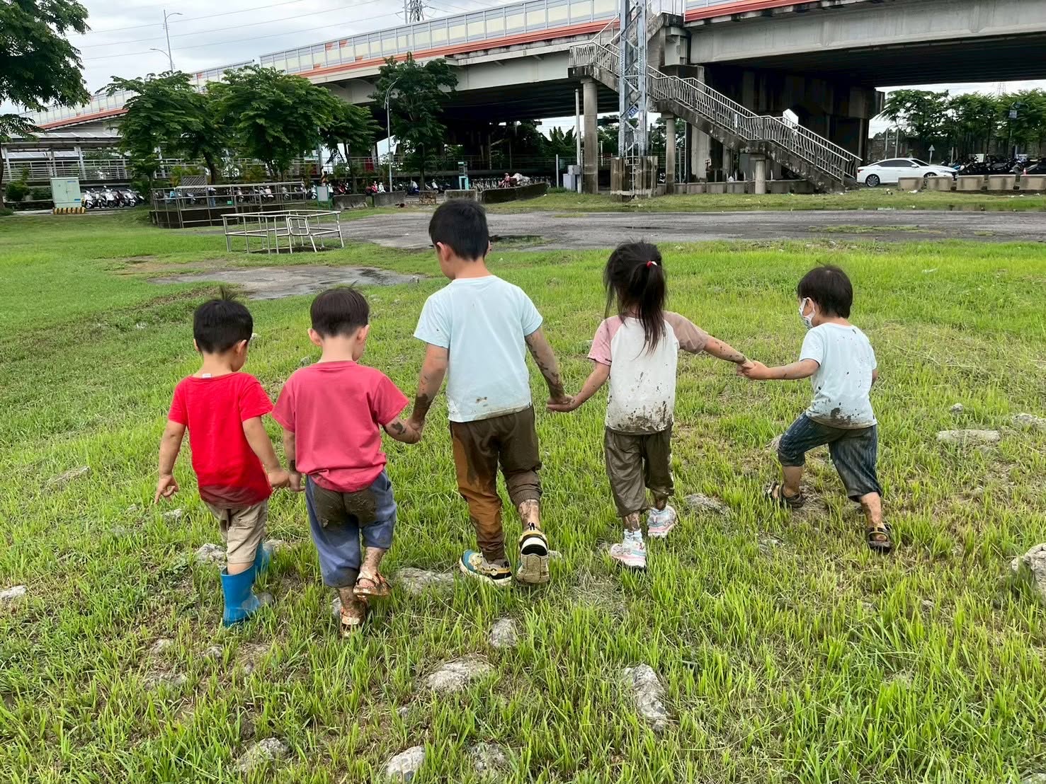 五位孩子牽著手走過草地,衣服上留著泥水探索的痕跡